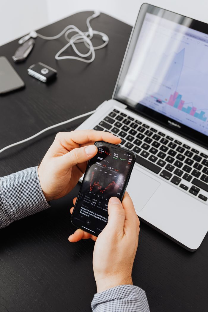 Mastering the First Impression: Your intriguing post title goes here Hands holding smartphone displaying stock charts by a laptop, showing market analysis.