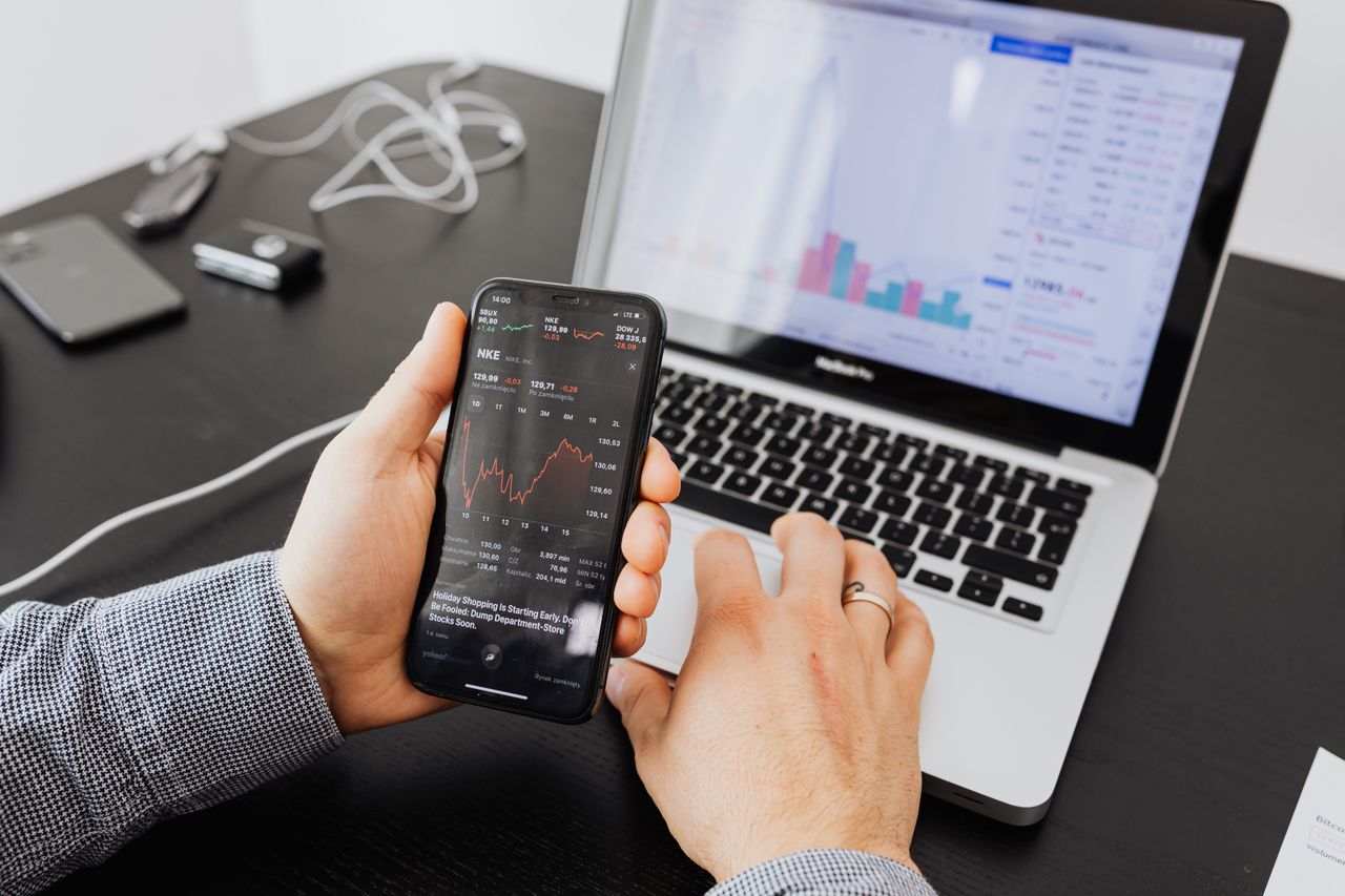 services-img Person analyzes stock data with a smartphone and laptop, indoors.